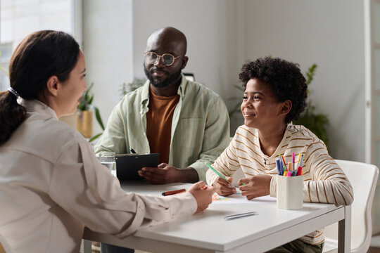 Portrait of smiling young boy talking to friendly doctor or social worker at desk in office, copy space