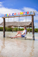 happy tourist blondie woman with long hair on a swing in the water of the tropical bay in sea shore