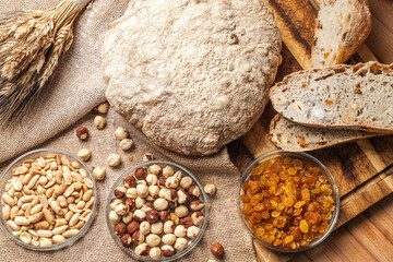 Bread with the addition of hazelnuts, peanuts and raisins in a cut and a whole loaf. on a wooden board with a bunch of wheat.