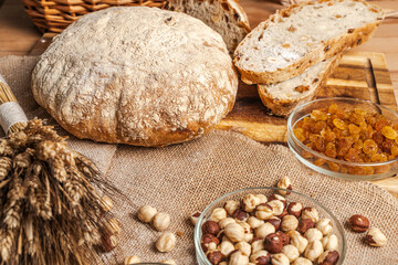 Homemade freshly baked bread with nuts and raisins, a whole loaf and sliced slices on a wooden table with ears of wheat.