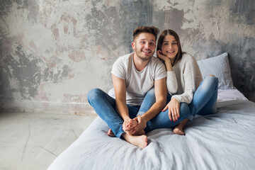 young happy smiling couple sitting on bed at home