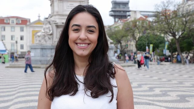 Happy young portuguese girl smiling at camera standing at Plaza del Rossio in Lisbon, Portugal. Joyful portrait of beautiful brunette woman feeling positive showing toothy smile.