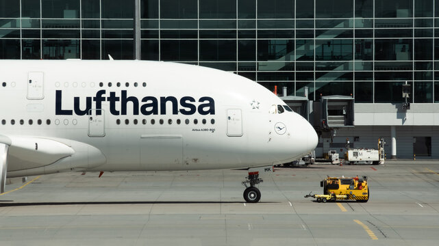 MUNICH, GERMANY - April 27: Close up of Airbus A380 cabin and nose gear with livery of Lufthansa airlines at Munich Airport. Big passenger aircraft and towing truck next to terminal building