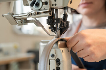 A woman tanner sews a leather belt on a sewing machine. 