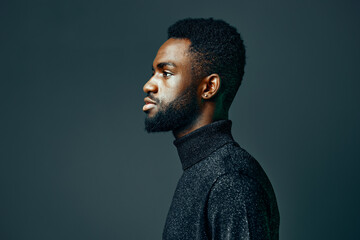 Confident young african american man with beard in a turtleneck, gazing thoughtfully against a dark...
