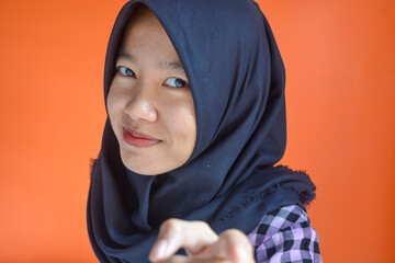 A friendly and successful Asian Muslim woman wearing a batik shirt with an orange background exclaimed excitedly while raising her two index fingers upwards, showing something.