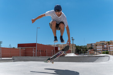 young skater wearing shorts does a trick with his skateboard in a skaterpark in a sunny day