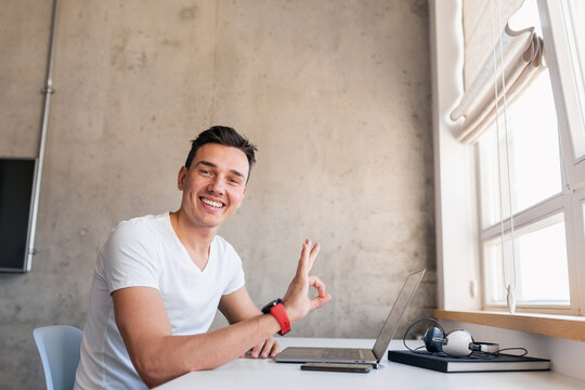 young handsome man in casual outfit sitting at table working on laptop, typing, freelancer at home - Powered by Adobe