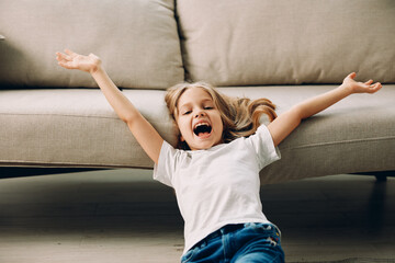 Little girl lying on the floor with arms outstretched, smiling in a cozy living room with a couch...