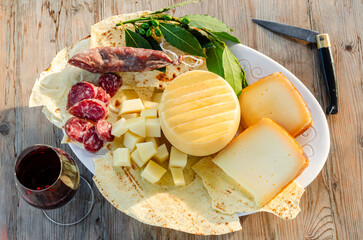 Vassoio con pecorino sardo e salsiccia secca di maiale, accompagnati da un calice di vino cannonau...