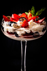 Strawberry dessert in a tall glass. Strawberries and blueberries with mascorpone and mint on a black background. Close-up. Selected focus.