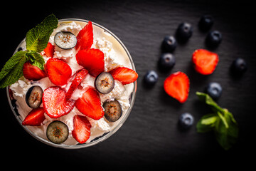 A beautiful berry dessert on a black background. Strawberries and blueberries with mascarpone cheese and mint.