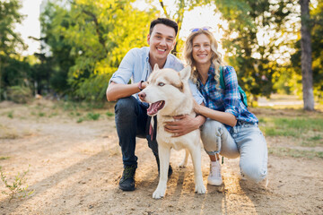 funny young stylish couple playing with dog in park