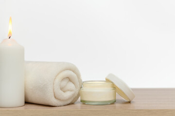 White candle, white towel, white glass container for cream.