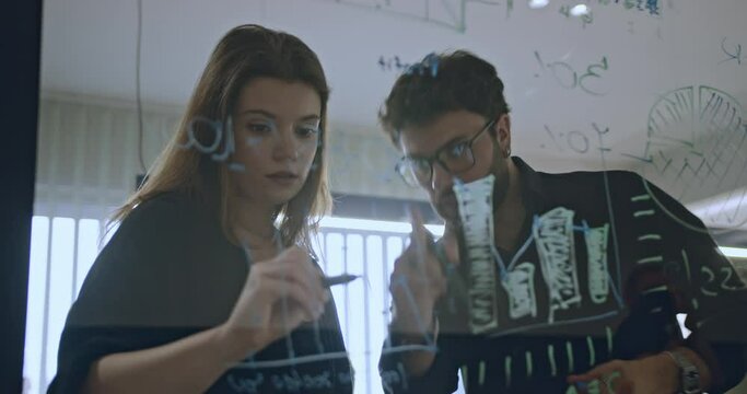 Business coworkers discussing new project solutions, financial planning, and strategy in a modern workspace using a transparent board.