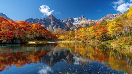 Obraz premium A picturesque scene of a mountain landscape in autumn, with vibrant fall foliage covering the hillsides. The clear blue sky contrasts with the golden and red leaves, while a calm river meanders