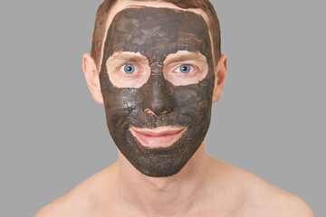 Black Clay Mask on Guy Face. Cosmetology man portrait with mud healthy scrub. Coal nature eco masque. Dermatology charcoal product. Home skin care routine. Skincare male treatment. Grey