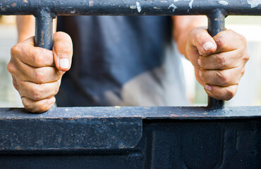 Image of a person's hand holding a cage in which they are confined.