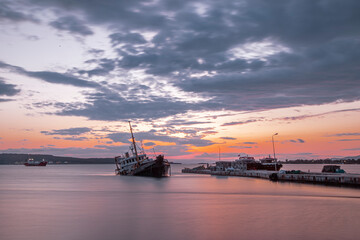 Fototapeta premium Sunken cargo ship lying on its side at sunset in Aliaga Bay, Izmir.
