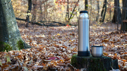 cup with tea. a thermos of tea, hot drink. thermos on an old tree stump. The concept of tourism,...