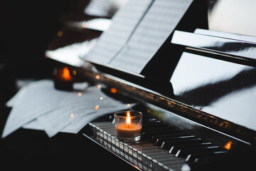 Piano keys with classical notes and burning candle over glowing lights in dark room at night.