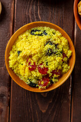 couscous with dried fruits in a wooden bowl next to the dogwood on the table