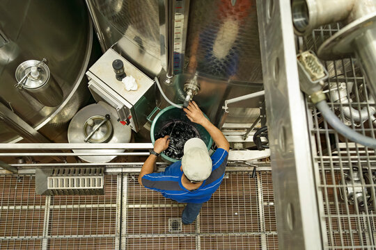 Winery worker managing fermentation tanks from above