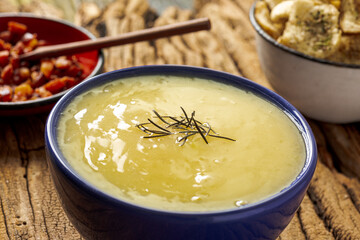 Delicious cassava cream (Caldo ou Creme de Mandioca) or cassava soup, typical of Brazilian cuisine, served in a blue porcelain bowl, on top of a typical rustic farm table, top view with selective focu