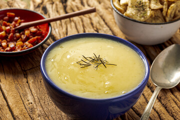 Delicious cassava cream (Caldo ou Creme de Mandioca) or cassava soup, typical of Brazilian cuisine, served in a blue porcelain bowl, on top of a typical rustic farm table, top view with selective focu