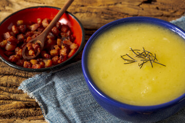 Delicious cassava cream (Caldo ou Creme de Mandioca) or cassava soup, typical of Brazilian cuisine, served in a blue porcelain bowl, on top of a typical rustic farm table, top view with selective focu