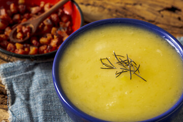 Delicious cassava cream (Caldo ou Creme de Mandioca) or cassava soup, typical of Brazilian cuisine, served in a blue porcelain bowl, on top of a typical rustic farm table, top view with selective focu