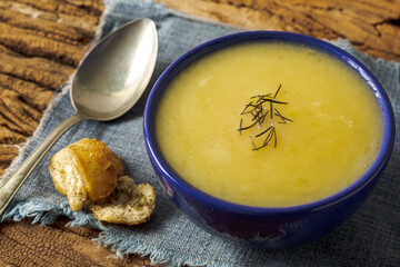Delicious cassava cream (Caldo ou Creme de Mandioca) or cassava soup, typical of Brazilian cuisine, served in a blue porcelain bowl, on top of a typical rustic farm table, top view with selective focu