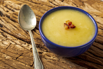 Delicious cassava cream (Caldo ou Creme de Mandioca) or cassava soup, typical of Brazilian cuisine, served in a blue porcelain bowl, on top of a typical rustic farm table, top view with selective focu