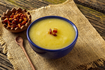 Delicious cassava cream (Caldo ou Creme de Mandioca) or cassava soup, typical of Brazilian cuisine, served in a blue porcelain bowl, on top of a typical rustic farm table, top view with selective focu