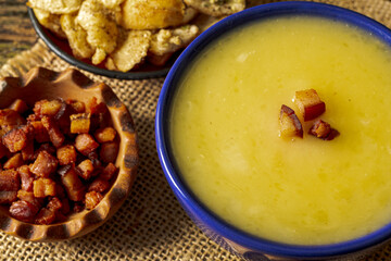 Delicious cassava cream (Caldo ou Creme de Mandioca) or cassava soup, typical of Brazilian cuisine, served in a blue porcelain bowl, on top of a typical rustic farm table, top view with selective focu