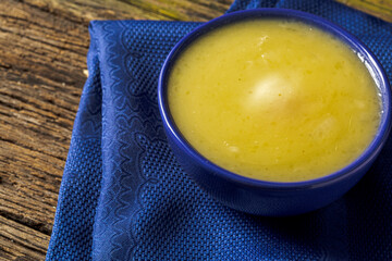Delicious cassava cream (Caldo ou Creme de Mandioca) or cassava soup, typical of Brazilian cuisine, served in a blue porcelain bowl, on top of a typical rustic farm table, top view with selective focu