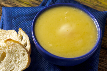 Delicious cassava cream (Caldo ou Creme de Mandioca) or cassava soup, typical of Brazilian cuisine, served in a blue porcelain bowl, on top of a typical rustic farm table, top view with selective focu