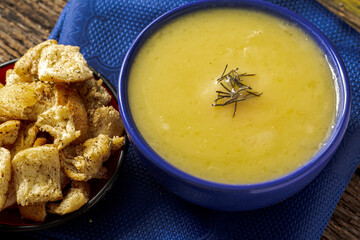 Delicious cassava cream (Caldo ou Creme de Mandioca) or cassava soup, typical of Brazilian cuisine, served in a blue porcelain bowl, on top of a typical rustic farm table, top view with selective focu