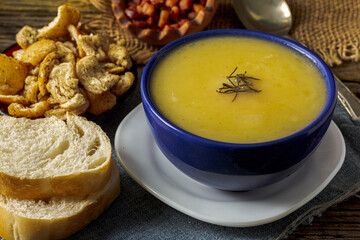 Delicious cassava cream (Caldo ou Creme de Mandioca) or cassava soup, typical of Brazilian cuisine, served in a blue porcelain bowl, on top of a typical rustic farm table, top view with selective focu