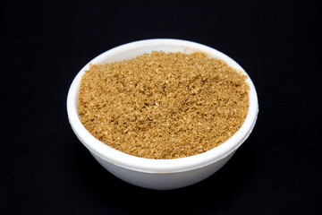 coriander seeds powder in white bowl, isolated in black background