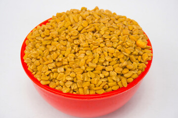 Fenugreek Split seeds, known as Methi Kuria, are cracked fenugreek seeds frequently utilized in Indian pickle recipes, in red bowl isolated on white background