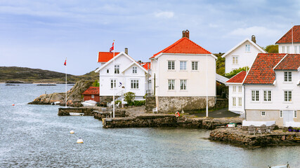 Traditional white wooden houses with red-tiled roofs by waterfront in beautiful fishing village. Cold destinations travel trend. Farsund, Norway