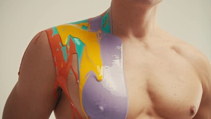 Colourful paint flowing over the man body close-up. Body art therapy with many various of paints. Painting on human body.