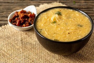 Caldo de Kenga Cassava broth with shredded chicken, typical Brazilian food known as (Caldo de Quenga), in a black pot on top of a rustica with a spoon and slices of bread,  with selective focus