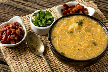 Caldo de Kenga Cassava broth with shredded chicken, typical Brazilian food known as (Caldo de Quenga), in a black pot on top of a rustica with a spoon and slices of bread,  with selective focus