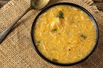 Caldo de Kenga Cassava broth with shredded chicken, typical Brazilian food known as (Caldo de Quenga), in a black pot on top of a rustica with a spoon and slices of bread,  with selective focus