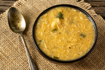 Caldo de Kenga Cassava broth with shredded chicken, typical Brazilian food known as (Caldo de Quenga), in a black pot on top of a rustica with a spoon and slices of bread,  with selective focus