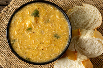Caldo de Kenga Cassava broth with shredded chicken, typical Brazilian food known as (Caldo de Quenga), in a black pot on top of a rustica with a spoon and slices of bread,  with selective focus