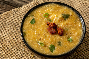 Caldo de Kenga Cassava broth with shredded chicken, typical Brazilian food known as (Caldo de Quenga), in a black pot on top of a rustica with a spoon and slices of bread,  with selective focus