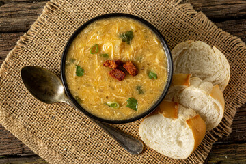 Caldo de Kenga Cassava broth with shredded chicken, typical Brazilian food known as (Caldo de Quenga), in a black pot on top of a rustica with a spoon and slices of bread,  with selective focus